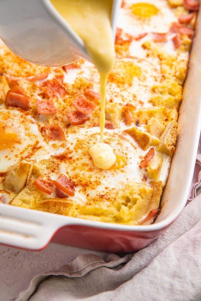 Hollandaise sauce pouring from a ramekin onto a breakfast casserole