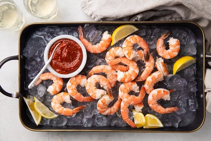 Black platter with boiled shrimp, shrimp cocktail sauce, ice, and lemon.