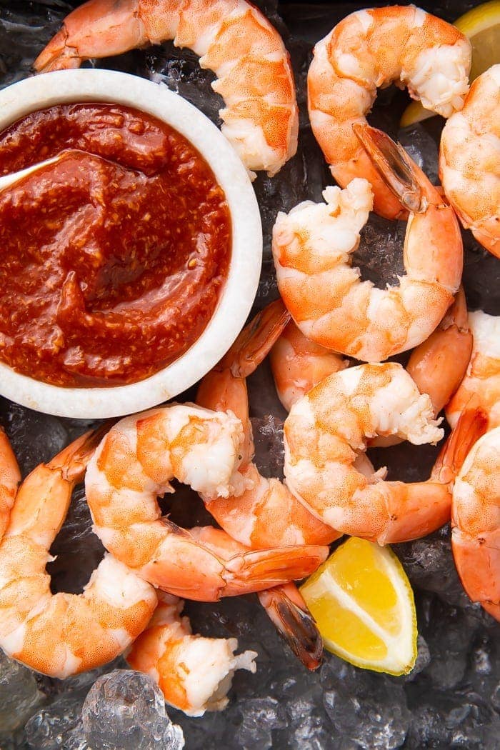 Shrimp cocktail sauce in a white ramekin on a black platter surrounded by peeled shrimp