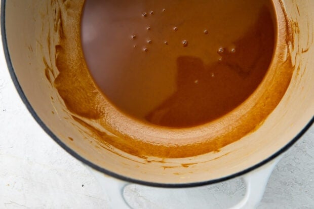Rich, brown liquid roux in heavy saucepan on a white background