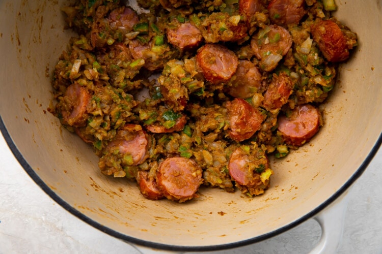 Chopped vegetables and andouille sausage mixed in a roux in a heavy pan