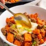 A spoon dipped into a white bowl of sweet potato hash