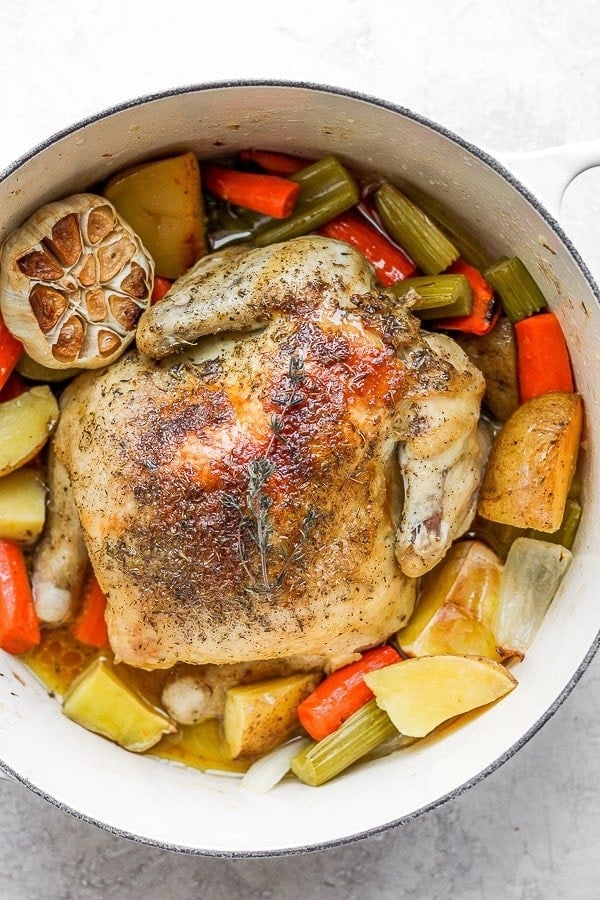 Dutch oven with a whole chicken, garlic, and vegetables