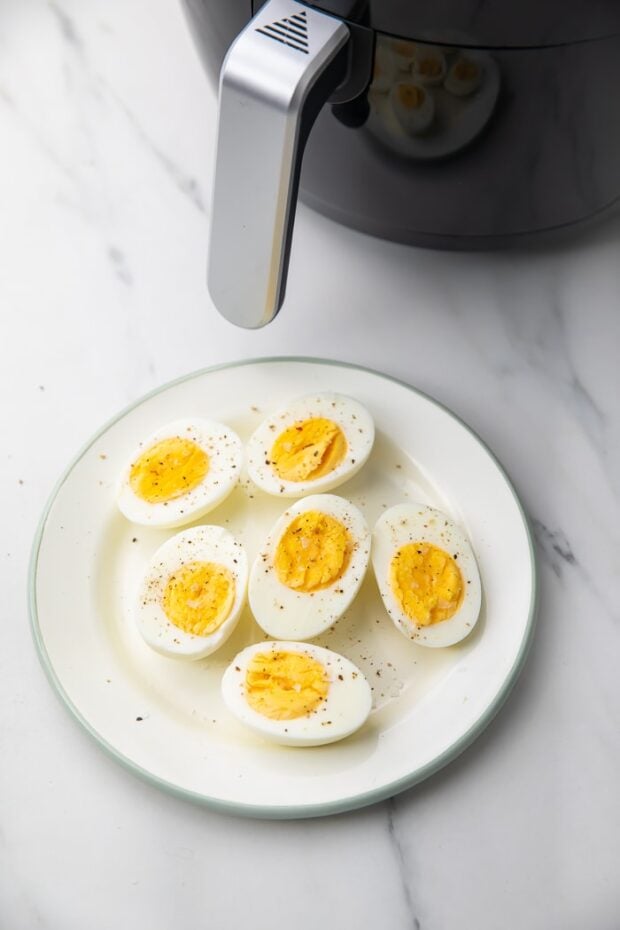 Hard boiled eggs on a white plate next to an air fryer