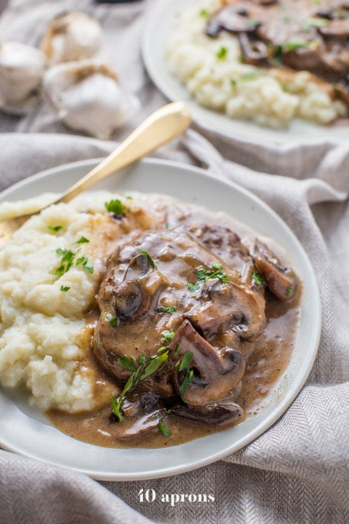 Salisbury steak and mashed potatoes on a white plate sitting on a white tablecloth