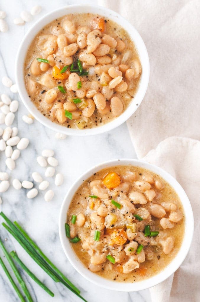 Two white bowls of vegetarian Instant Pot white bean soup with veggies