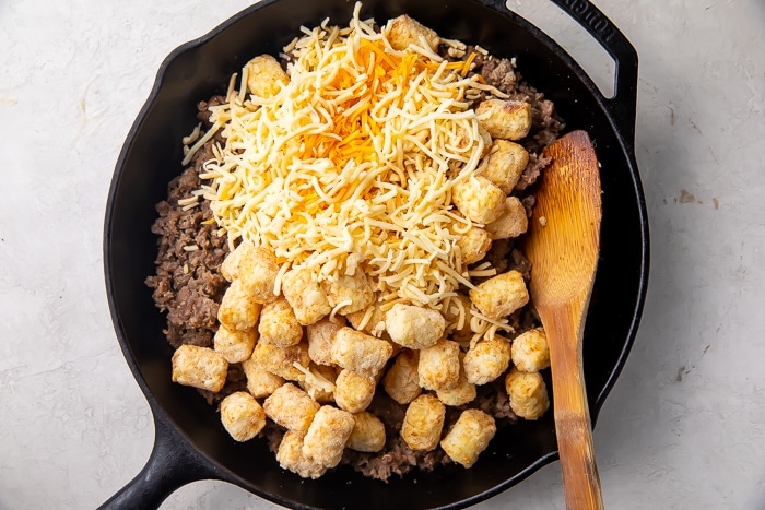 Cast iron skillet with shredded cheese, sausage, and tater tots