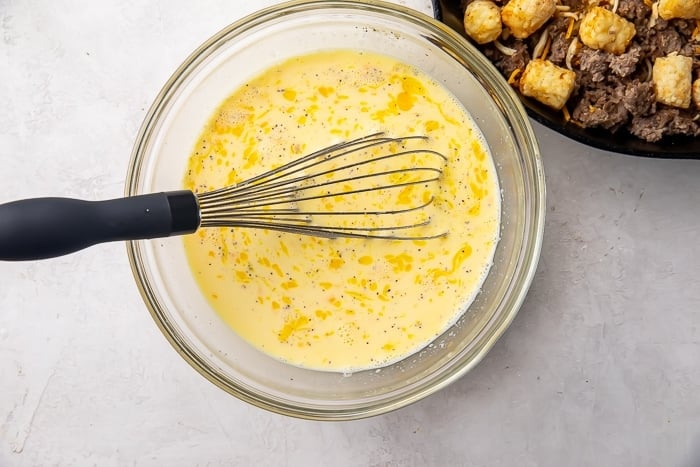 Glass mixing bowl with scrambled eggs, milk, and seasoning
