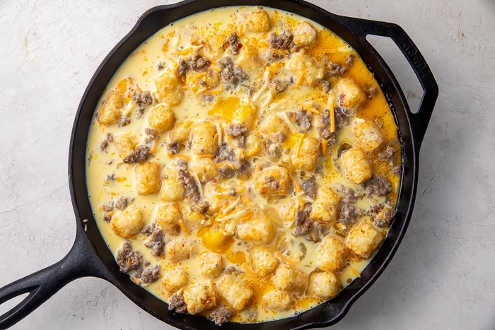 Uncooked tater tot breakfast casserole in a cast iron skillet