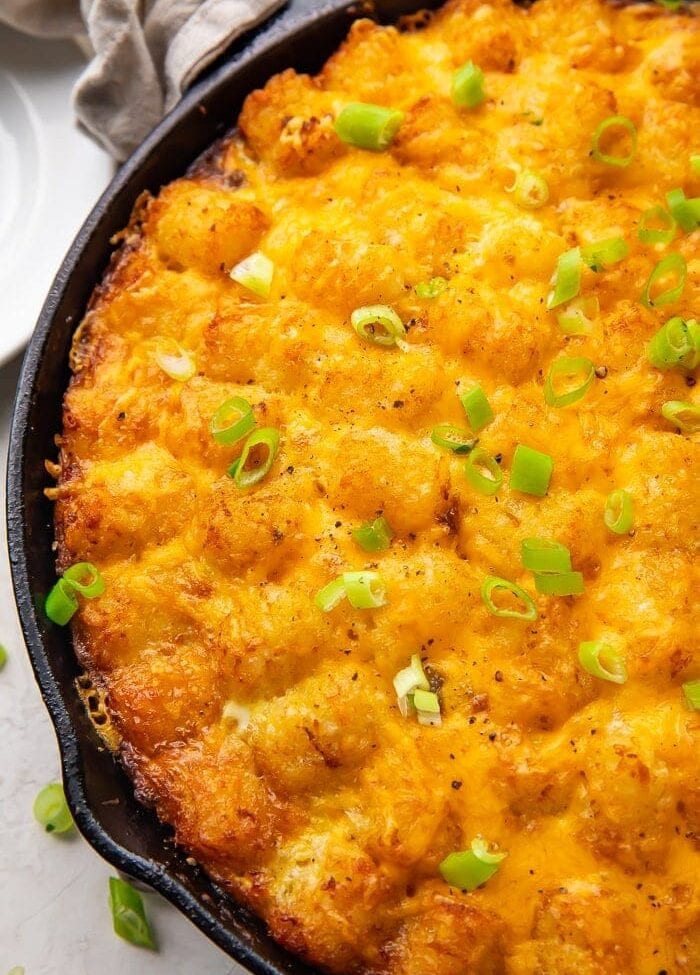 Cast iron skillet holding a tater tot breakfast casserole with cheese, sausage, and eggs, topped with chives