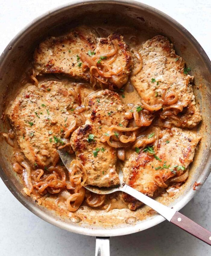 One large skillet holding 4 porkchops and onions with a sauce