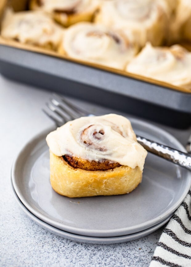 Keto cinnamon roll on a blue plate in front of a pan of cinnamon rolls