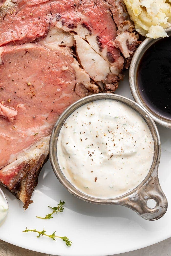 A side of horseradish sauce next to prime rib on a white plate