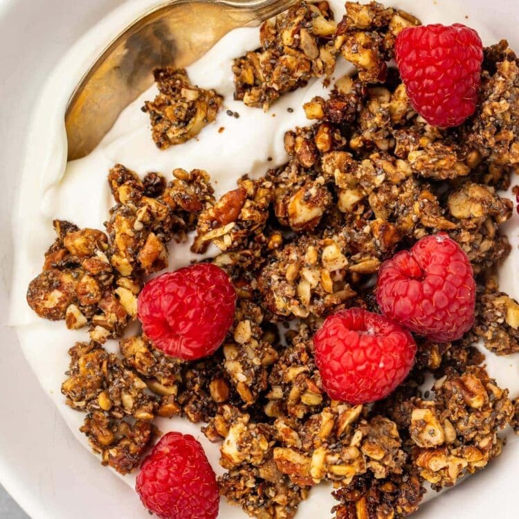 Keto granola on top of a bowl of yogurt garnished with raspberries