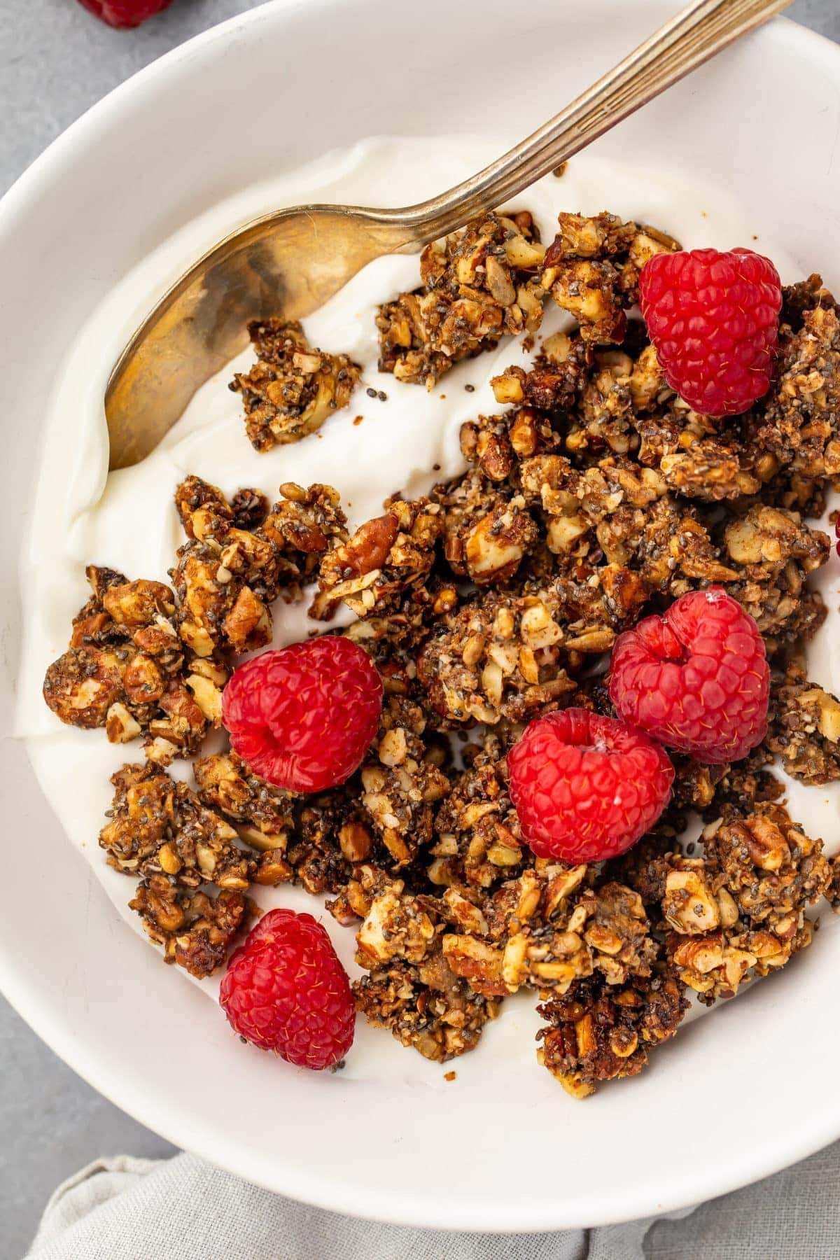 Keto granola on top of a bowl of yogurt garnished with raspberries