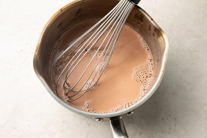 Cocoa powder and heavy cream mixture for keto hot chocolate in a saucepan with a whisk