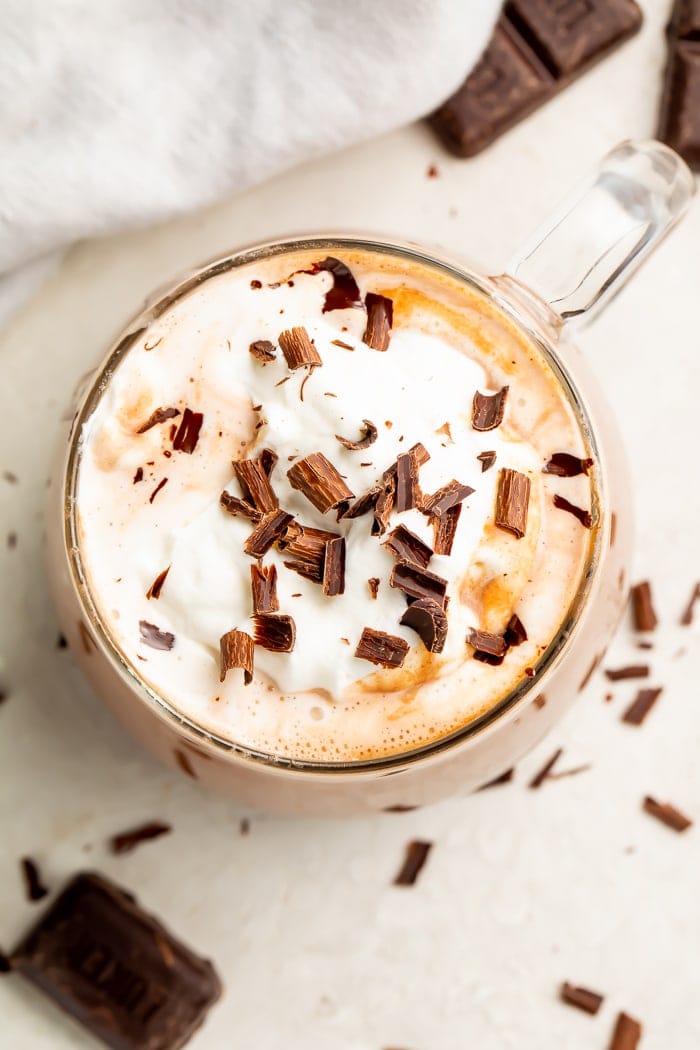 Aerial photo of keto hot chocolate with whipped cream and chocolate shavings in a glass mug on a white counter
