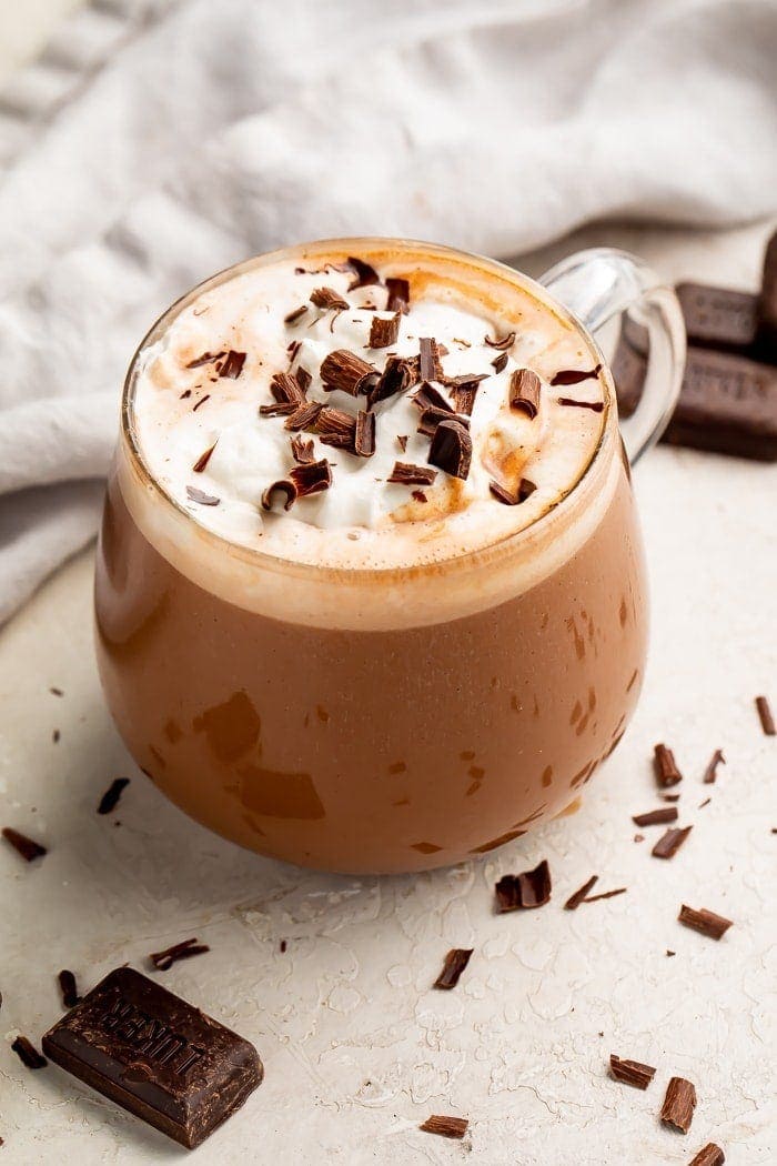 Zoomed out photo of keto hot chocolate with whipped topping and chocolate shavings in a glass mug