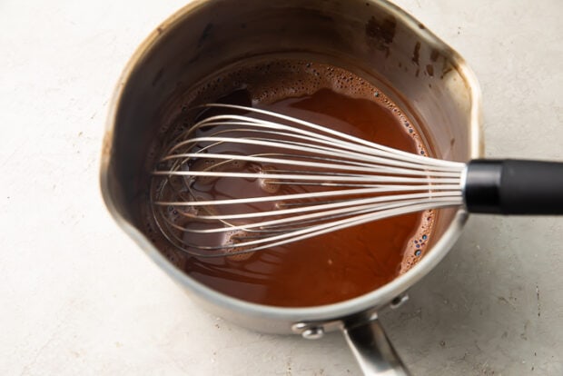 Hot water and cocoa powder in a silver saucepan with whisk for keto hot chocolate