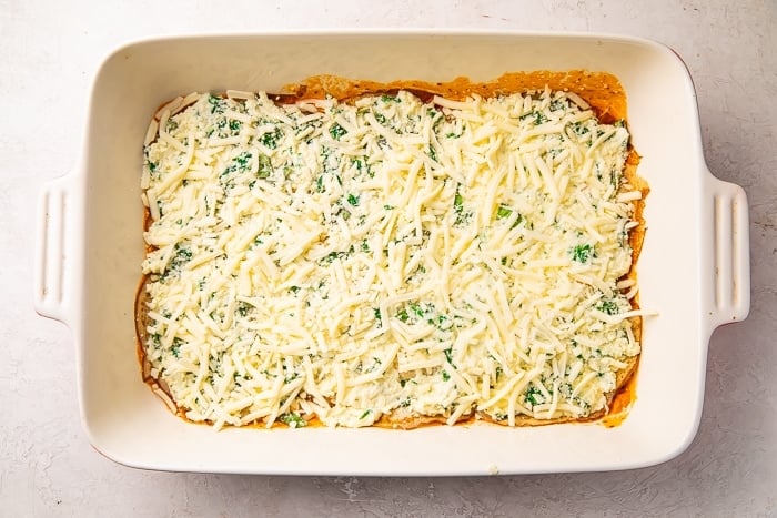 Baking dish with keto lasagna meat sauce, egg thins, spinach and ricotta cheese mixture, and mozzarella