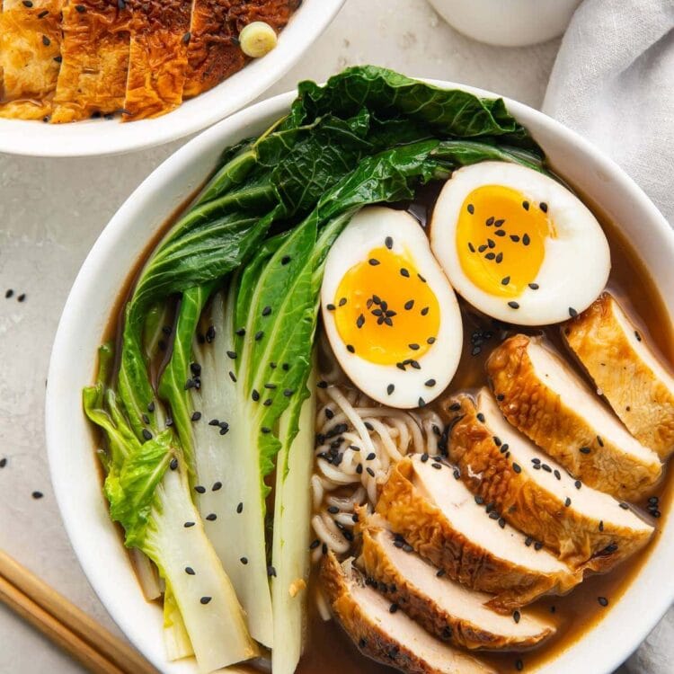 A white bowl of keto ramen with shirataki noodles, ramen eggs, chicken, and bok choy