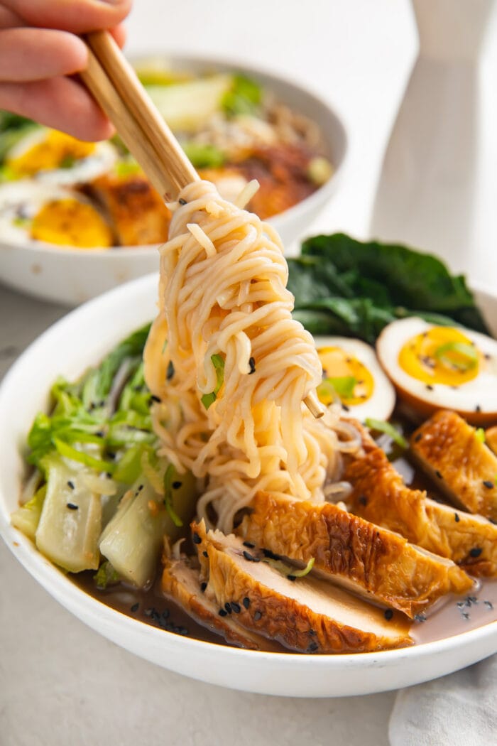 A hand holding chopsticks lifting shirataki noodles out of a white bowl of keto ramen