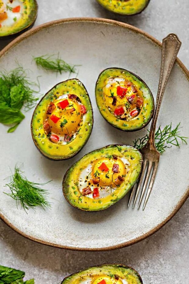 Avocado halves filled with eggs and veggies on an off-white plate