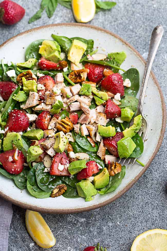 Strawberry avocado spinach salad on a white plate with a fork