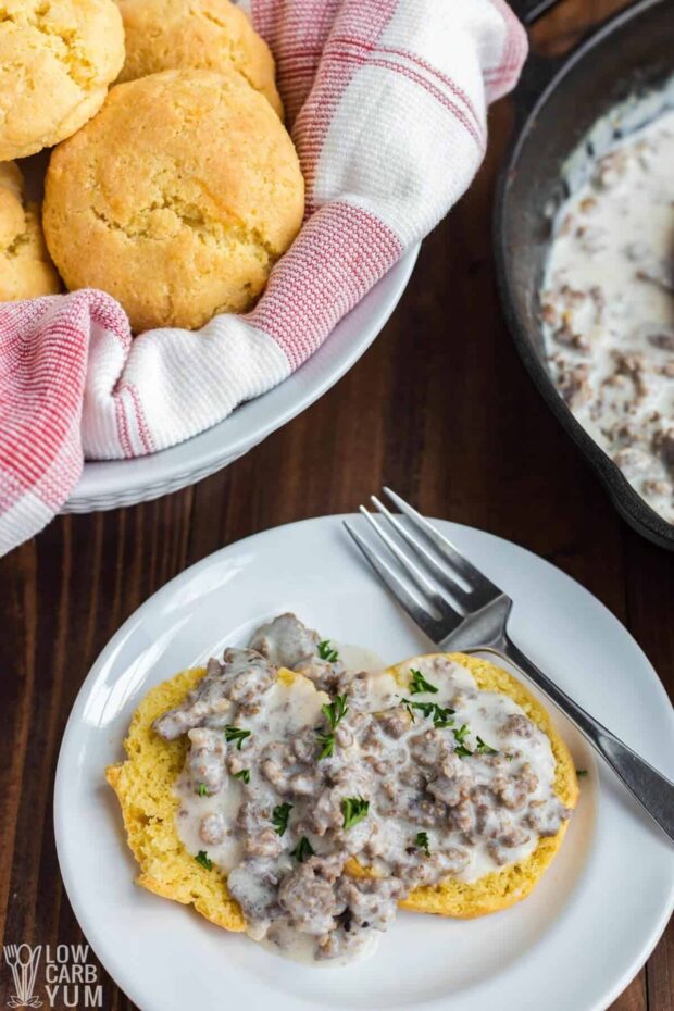 Keto biscuits with sausage gravy on a white plate in front of a basket of biscuits