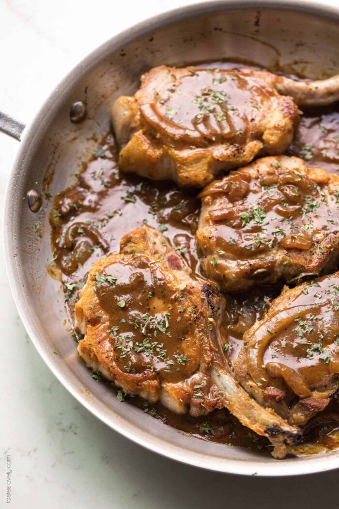 Balsamic mustard pork chops in a brown skillet on a white background