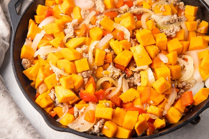 Sweet potato, onion, bell pepper, ground sausage in a cast iron skillet