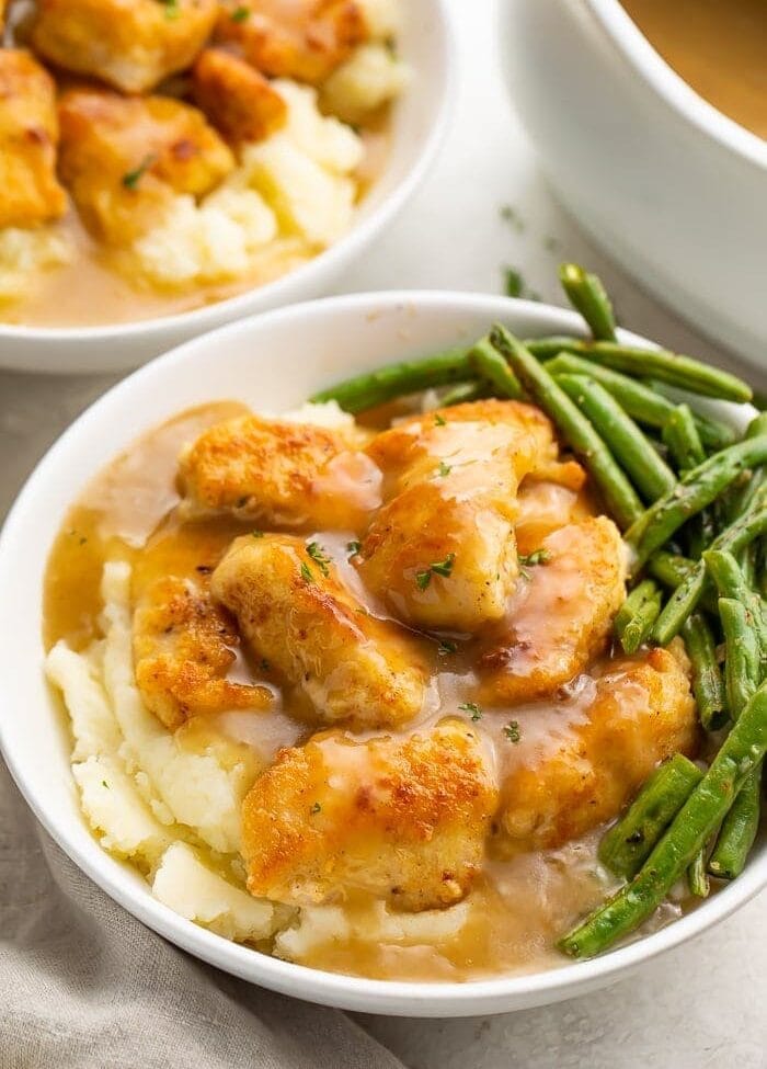 Whole30 fried chicken and mashed potatoes with gravy and green beans in a white ceramic bowl