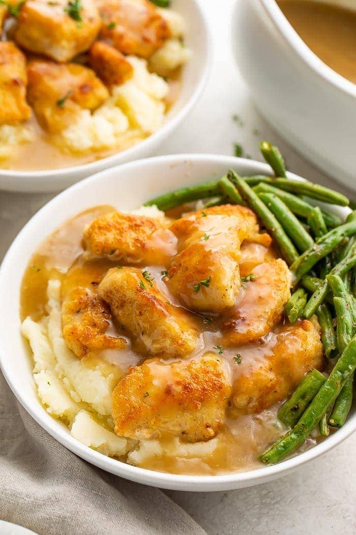 Whole30 fried chicken and mashed potatoes with gravy and green beans in a white ceramic bowl