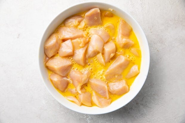 Raw chicken bites in a large bowl of beaten egg