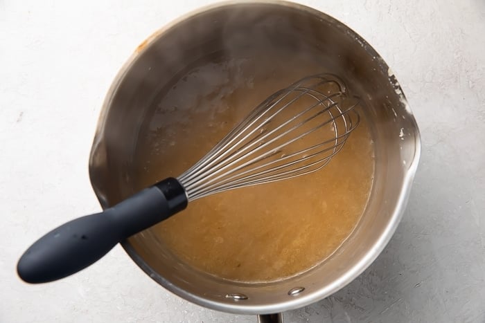 Silver saucepan with chicken gravy and a whisk