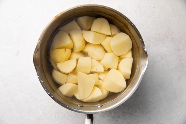 Raw potato chunks in a silver saucepan on a white counter
