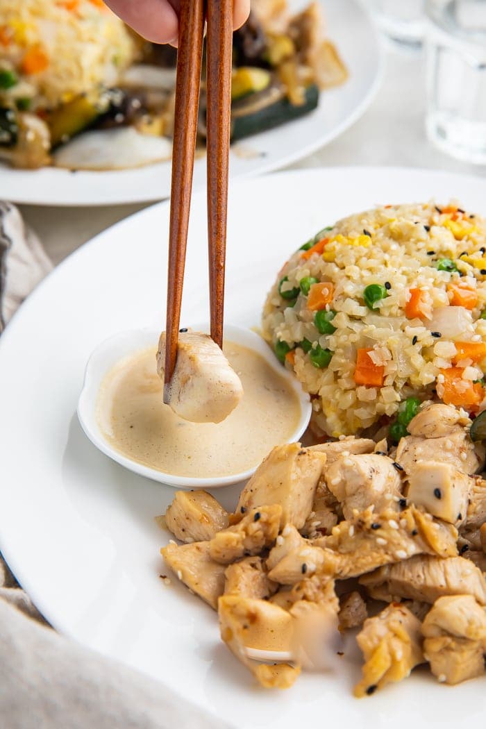 Whole30 hibachi chicken dipped in mustard sauce next to a scoop of whole30 fried cauliflower rice