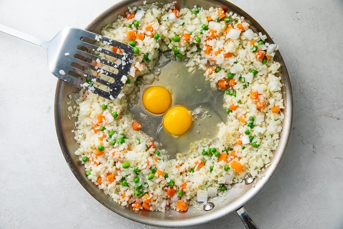 Frozen vegetables surrounding two eggs in a large wok with a spatula