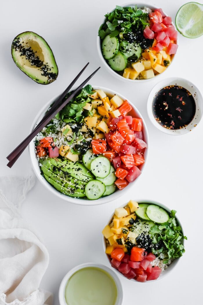 3 white bowls with veggies, sushi grade salmon, and sushi grade tuna