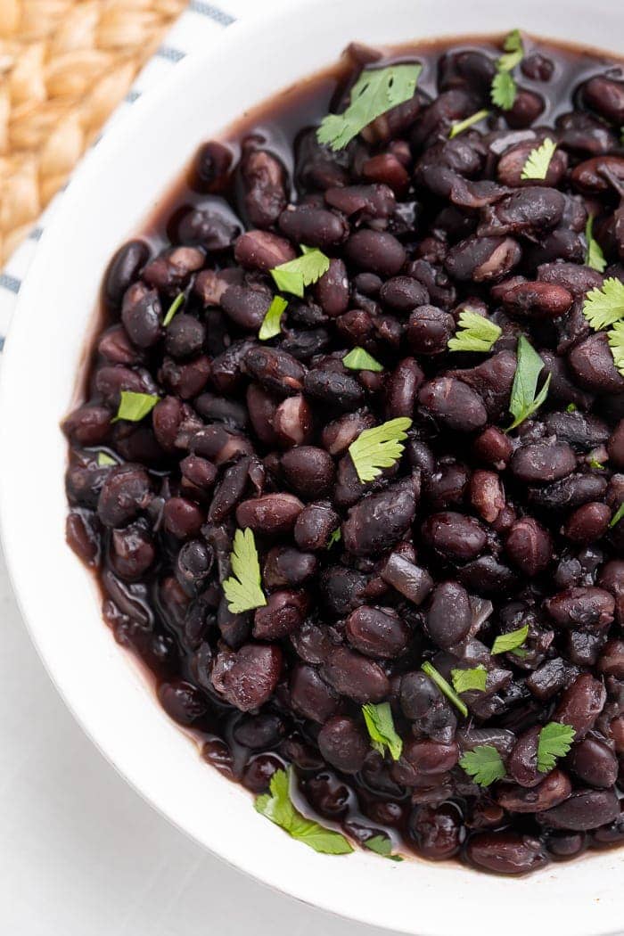 Half of a white bowl full of thick black beans and garnish