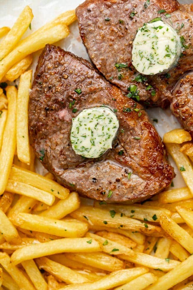 Two air fried steaks topped with herb butter with a side of fries