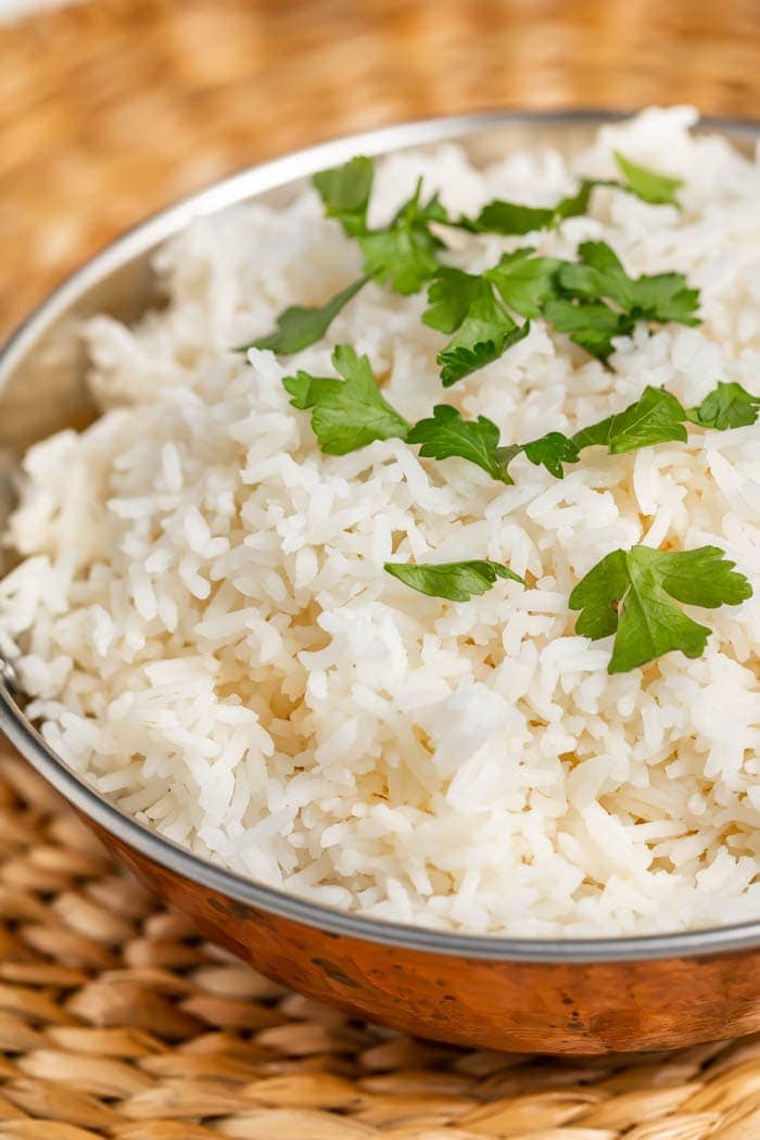 A silver mixing bowl of basmati rice and garnish on a woven placemat