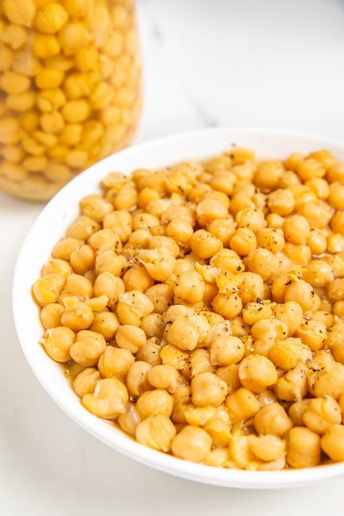 A partial bowl of chickpeas next to a jar of chickpeas on a white background