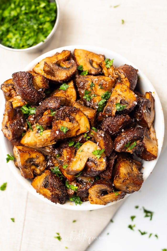 A white bowl of air fried mushrooms on a white countertop