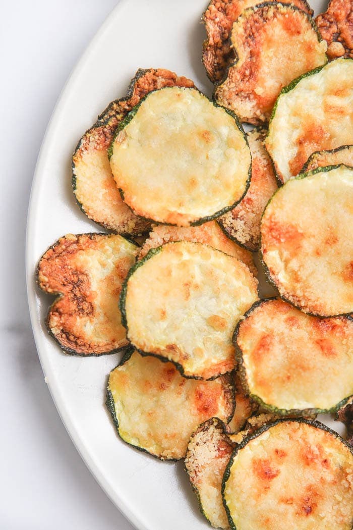 Air fried zucchini chips on a white plate on a white table