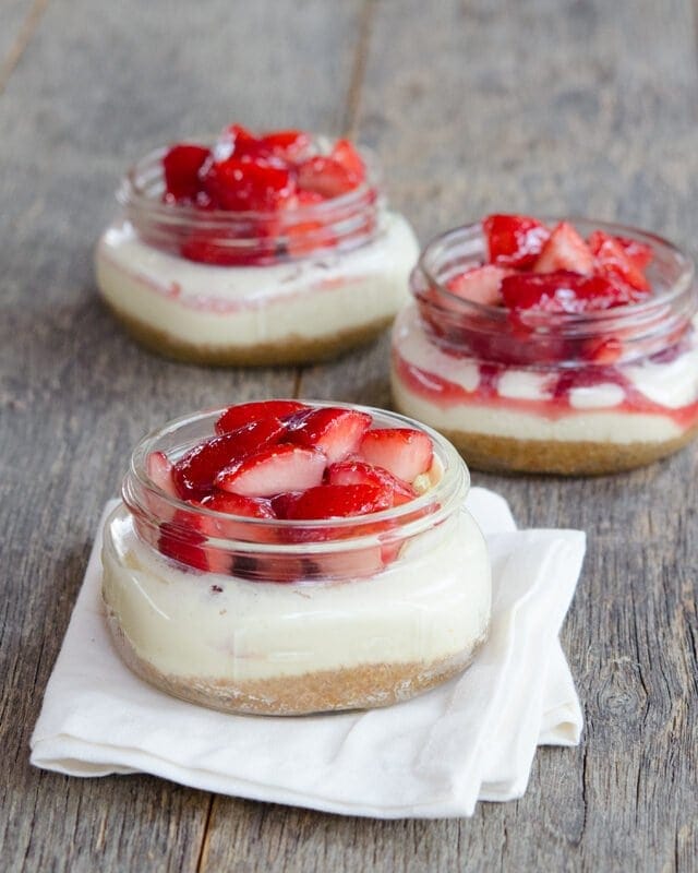 3 mason jars with crust, cheesecake, and strawberries. Foreward jar is sitting on a white napkin