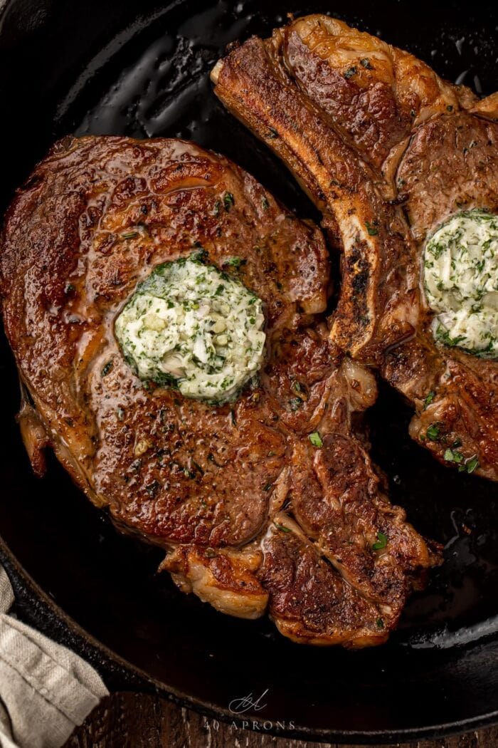 2 bone-in ribeye topped with garlic-herb butter in a cast iron pan