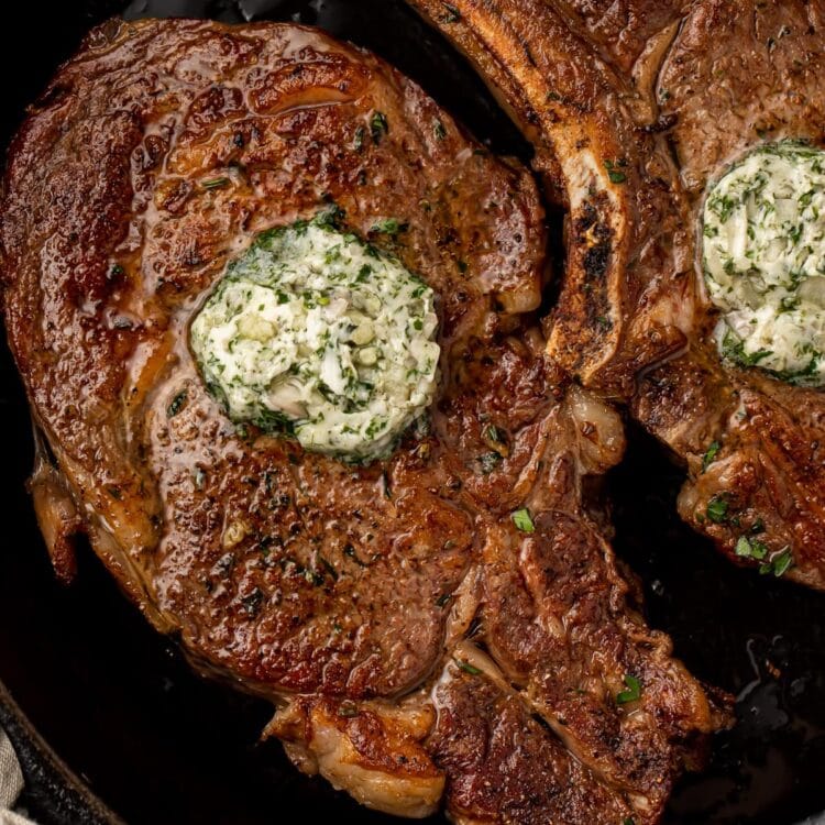 2 bone-in ribeye topped with garlic-herb butter in a cast iron pan