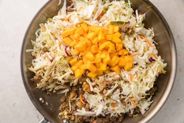 Ground pork, coleslaw, mango, and coconut aminos in a silver saucepan