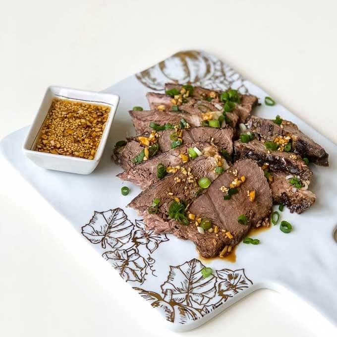 A marble platter with sesame beef and a square bowl of dipping sauce